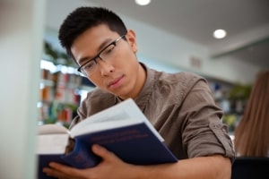Asian Male Student with Specs Reading Book