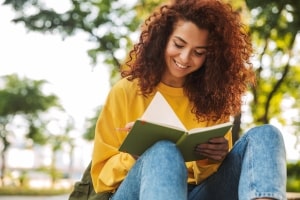 Curly Girl Student Sitting Outdoors Writing Notes in Notebook
