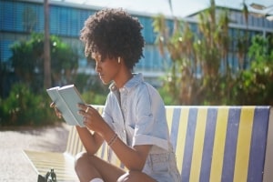 Girl Reading Book Sitting on Bench in College Campus