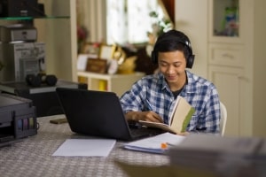 Young Student Writing Notes While Learning Online at Home
