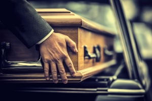 Funeral Director Carefully Loading A Coffin into A Black Hearse