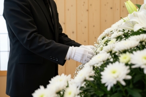 A funeral director in white gloves carefully arranging white lilies and chrysanthemums, reflecting the compassionate and detail-oriented nature of funeral service work.
