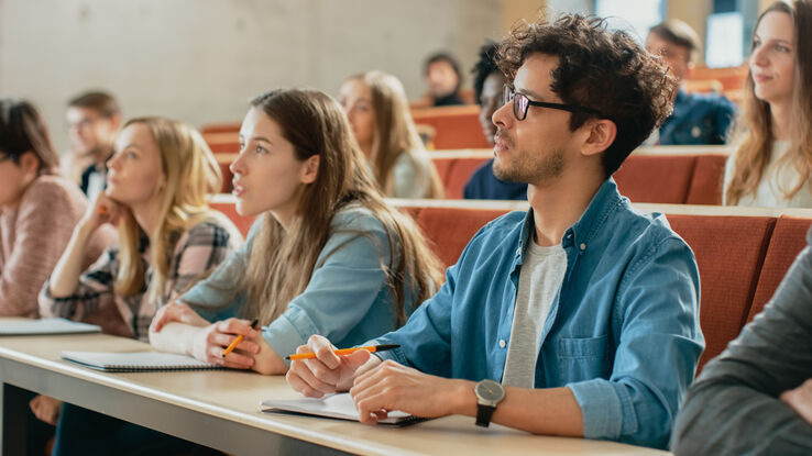 Multi Ethnic Students Listening to a Lecturer and Writing in Notebooks