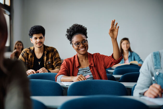 Happy black student raising her hand to ask question during class at university