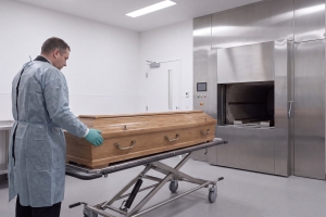 Crematory Operator Carrying a Wooden Coffin Towards Cremation Furnace
