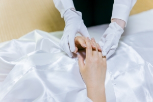 Embalmer Wearing Gloves Clasping the Hands of Deceased